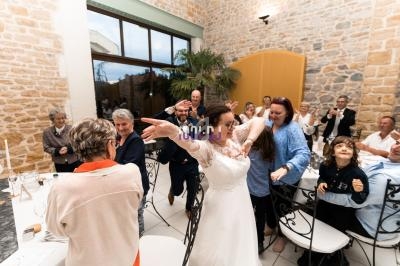 Une mariée danse entourée d'invités souriants dans une salle en pierre avec de grandes fenêtres.