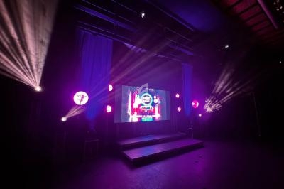 Scène éclairée avec des projecteurs colorés et un écran affichant des graphismes lumineux dans une salle sombre.