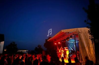 Scène extérieure éclairée en rouge avec un groupe de musique jouant devant un public en soirée.