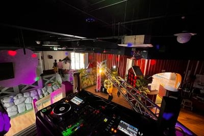 Vue depuis une cabine de DJ avec platines, éclairages colorés et piste de danse dans une salle sombre.