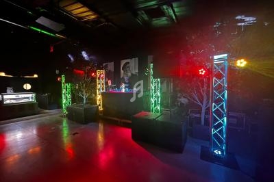 Salle sombre avec un DJ en arrière-plan, éclairée par des projecteurs colorés sur des structures métalliques.