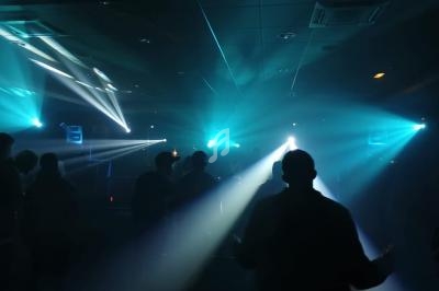 Personnes dans une salle sombre éclairée par des faisceaux lumineux bleus et blancs lors d'un événement.