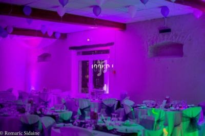 Salle de réception décorée avec des tables dressées, des ballons suspendus et un éclairage violet.