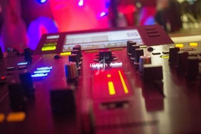 Table de mixage avec curseurs, boutons et lumières colorées, utilisée dans un environnement de musique ou de DJing.