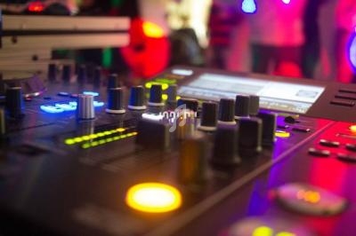 Table de mixage éclairée avec des boutons et des curseurs, entourée de lumières colorées en arrière-plan flou.