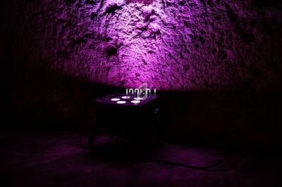 Projecteur LED diffusant une lumière violette sur un mur texturé dans un environnement sombre.
