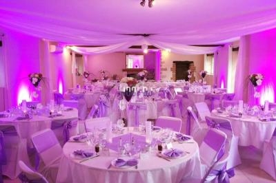Salle de réception décorée avec des nappes blanches, des rubans violets et des arrangements floraux élégants.