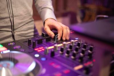 Main ajustant les réglages sur une table de mixage audio éclairée par des lumières violettes.