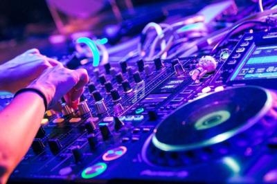 Main posée sur une table de mixage avec des lumières colorées en arrière-plan.