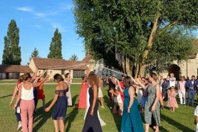 Un groupe de personnes dansant en cercle sur une pelouse, sous un ciel bleu, près d'arbres et de bâtiments.