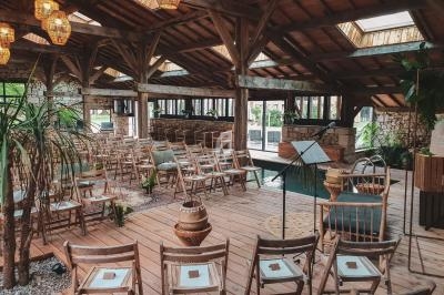 Salle en bois avec des chaises disposées pour un événement, entourée de plantes et éclairée par des lanternes suspendues.