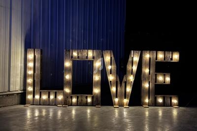 Lettres géantes en bois formant le mot ’LOVE’, éclairées par des ampoules, posées sur un sol en béton.