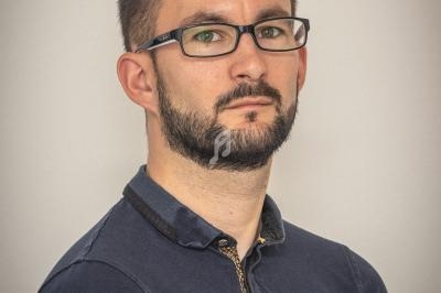 Homme portant des lunettes et une chemise bleu foncé, regardant face à l'objectif devant un fond neutre.