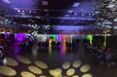 Salle de réception avec éclairage coloré et motifs lumineux au sol, des tables occupées par des convives.