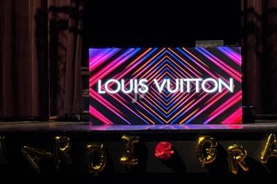 Bureau de DJ avec écran lumineux affichant ’Louis Vuitton’, décoré de ballons formant ’Mardi Gras’.