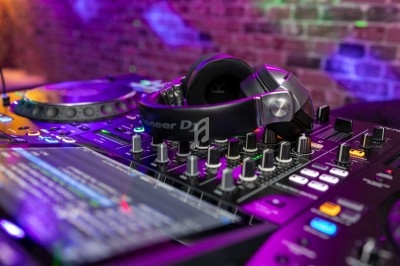 Table de mixage avec casque audio posé dessus, entourée de lumières colorées et d'un mur en briques en arrière-plan.