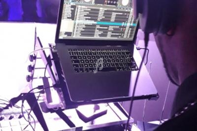 Un DJ utilise un ordinateur portable avec un logiciel de mixage, entouré d'équipements audio sous une lumière violette.