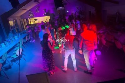 Groupe de personnes dans une salle éclairée par des lumières colorées, dansant et socialisant lors d'un événement festif.
