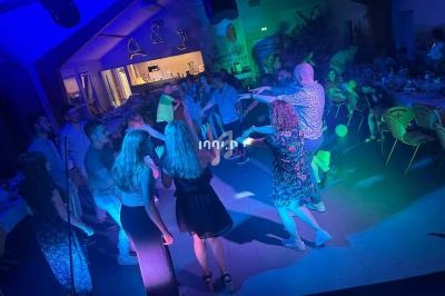 Des personnes dansent en cercle sur une piste éclairée par des lumières colorées lors d'une fête en intérieur.