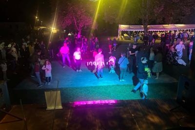 Personnes dansant et socialisant en soirée en plein air, éclairées par des lumières colorées sous des arbres et une tente.