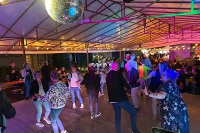 Des personnes dansent sous une structure couverte éclairée par des guirlandes lumineuses et une boule disco.