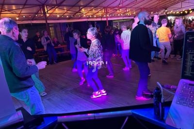 Des personnes dansent sous une tente éclairée par des guirlandes lumineuses lors d'une soirée festive.