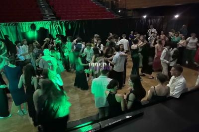 Des personnes dansent et discutent dans une salle de fête éclairée par des lumières vertes, avec des gradins en arrière-plan.