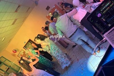 Des personnes dansent et discutent dans une salle éclairée par des lumières colorées, avec une table de DJ au premier plan.