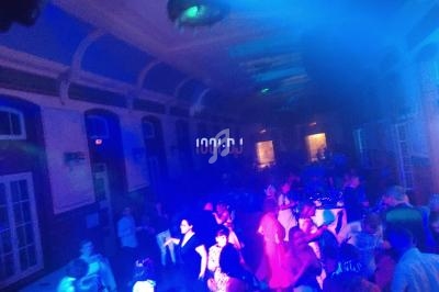 Personnes dansant sous des lumières colorées dans une salle avec de grandes fenêtres et un plafond voûté.