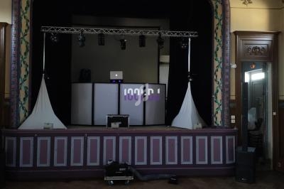 Scène avec une installation de DJ comprenant des lumières, un écran lumineux et des enceintes dans une salle décorée.