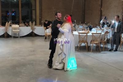 Un couple danse dans une salle de réception décorée, entouré de tables et de quelques invités.