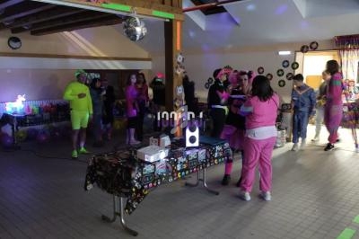 Personnes en tenue colorée dans une salle décorée pour une fête, avec table équipée de matériel audio et lumières.