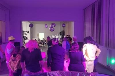 Des personnes déguisées participent à une fête dans une salle éclairée par des lumières violettes.