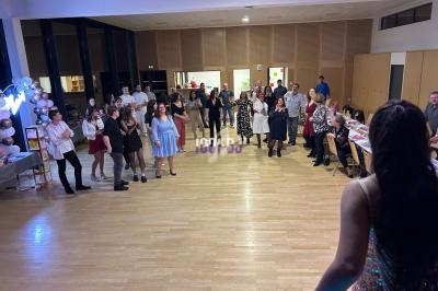 Une femme en robe scintillante s'adresse à un groupe de personnes réunies dans une salle décorée pour une fête.