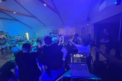 Groupe de personnes dans une salle éclairée par des lumières colorées, dansant près d'une table de mixage.