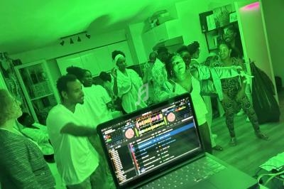 Des personnes dansent et s'amusent dans une pièce éclairée par une lumière verte, avec un ordinateur en premier plan.