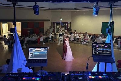 Un couple danse au centre d'une salle de réception, vu depuis une table de DJ équipée de matériel audio.
