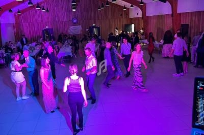 Des personnes dansent dans une salle éclairée de lumières colorées, avec des tables dressées en arrière-plan.