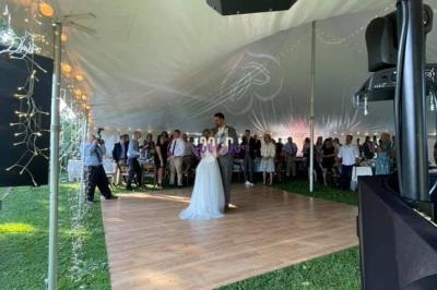 Un couple danse sous une tente blanche lors d'un mariage, entouré d'invités debout sur une pelouse.