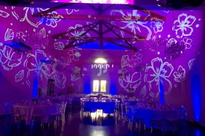 Salle de réception décorée avec des projections lumineuses de fleurs violettes et des tables dressées pour un événement.