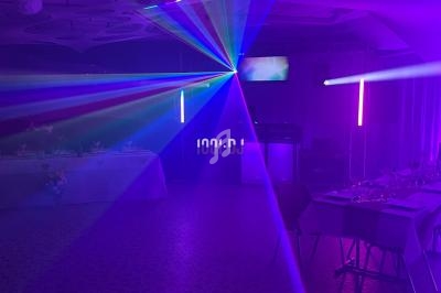 Salle de réception sombre avec des éclairages colorés et des lasers, tables dressées sur les côtés.