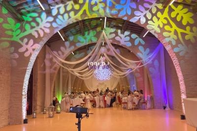 Salle voûtée décorée de voilages et lumières colorées, avec des invités assis à des tables rondes pour un événement.