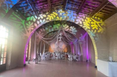 Salle voûtée décorée pour un événement, avec éclairages colorés, tables dressées et voilages suspendus.