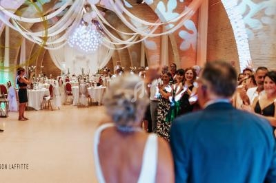 Salle de réception décorée pour un mariage, avec des invités applaudissant un couple au premier plan.