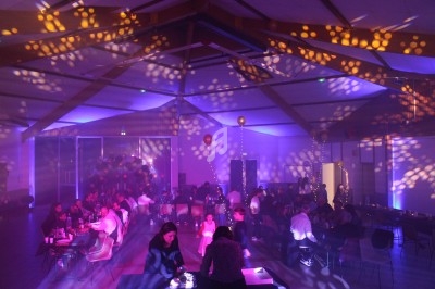 Salle de réception décorée avec des lumières colorées et des invités assis à des tables lors d'un événement festif.