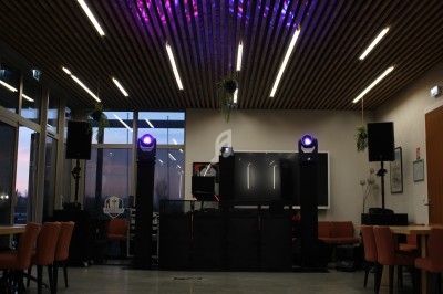Salle équipée de matériel de sonorisation et d'éclairage, avec des tables, des chaises et un plafond en bois.