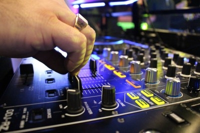 Main ajustant un fader sur une table de mixage audio éclairée par des lumières colorées.