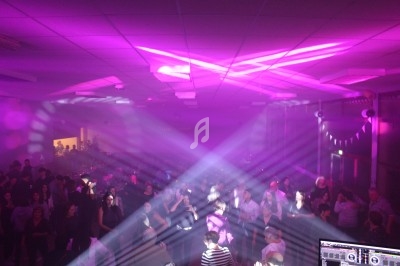 Salle comble avec des personnes dansant sous des éclairages violets et des jeux de lumière.