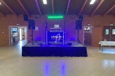 Scène de DJ avec platines, éclairage LED coloré et enceintes dans une salle aux murs en bois et plafond en poutres…