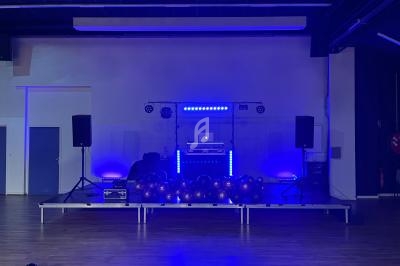 Scène éclairée en bleu avec équipement de DJ, haut-parleurs et ballons posés au sol dans une salle sombre.